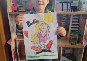 Jasio prezentuje pokolorowany przez siebie obrazek z lalką Barbie.