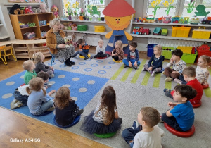 Dzieci siedzą w kole i słuchają opowiadania Pani Bibliotekarki.