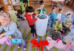 Dzieci piorą w pralce ubranka dla lalek i przypinają je klamerkami do sznurka.