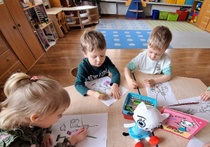 Dzieci kolorują przy stoliku obrazki konturowe przedstawiające sprzęty do sprzątania.