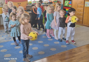 Dzieci stoją z piłkami ustawione w dwóch rzędach.