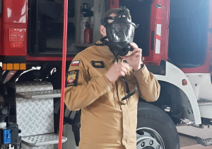 Strażak prezentuje dzieciom maskę służącą strażakom podczas gaszenia pożarów
