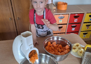 Zosia wrzuca marchewkę do robota kuchennego.