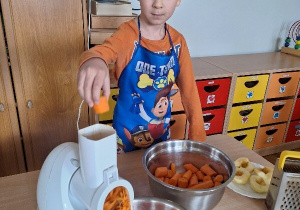 Karol wrzuca marchewkę do robota kuchennego.