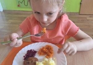 Oliwka zjada na obiad surówkę marchewkową, przygotowaną wspólnie z dziećmi podczas zajęć kulinarnych.