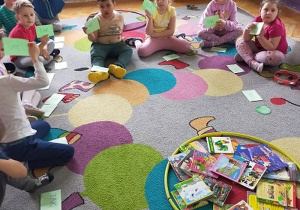 Dzieci siedzą na dywanie i pokazują kartki z odpowiedziami
