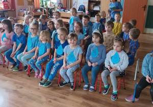 Dzieci ubrane na niebiesko siedzą na krzesełkach