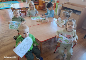 Dzieci kolorują przy stoliku obrazek konturowy "Drzewa".